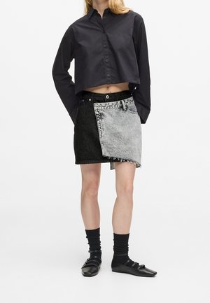 Chemise noire à boutons recadrée associée à une mini-jupe en jean bicolore, chaussettes noires et chaussures plates Mary Jane noires.