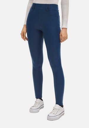 Leggings elásticos azul marino con una cintura alta, bolsillos laterales y una textura suave, complementados con zapatillas blancas.