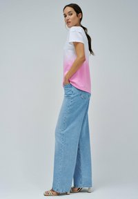 Camiseta ombre blanca y rosa con un corte holgado, combinada con jeans de pierna ancha en azul claro. Presenta mangas cortas y un bolsillo en el lateral.