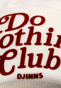 Weiße Strickmütze mit gerippter Textur, die in kräftigem Rot den Schriftzug "Do Nothing Club" und am unteren Ende "DJINNS" zeigt.