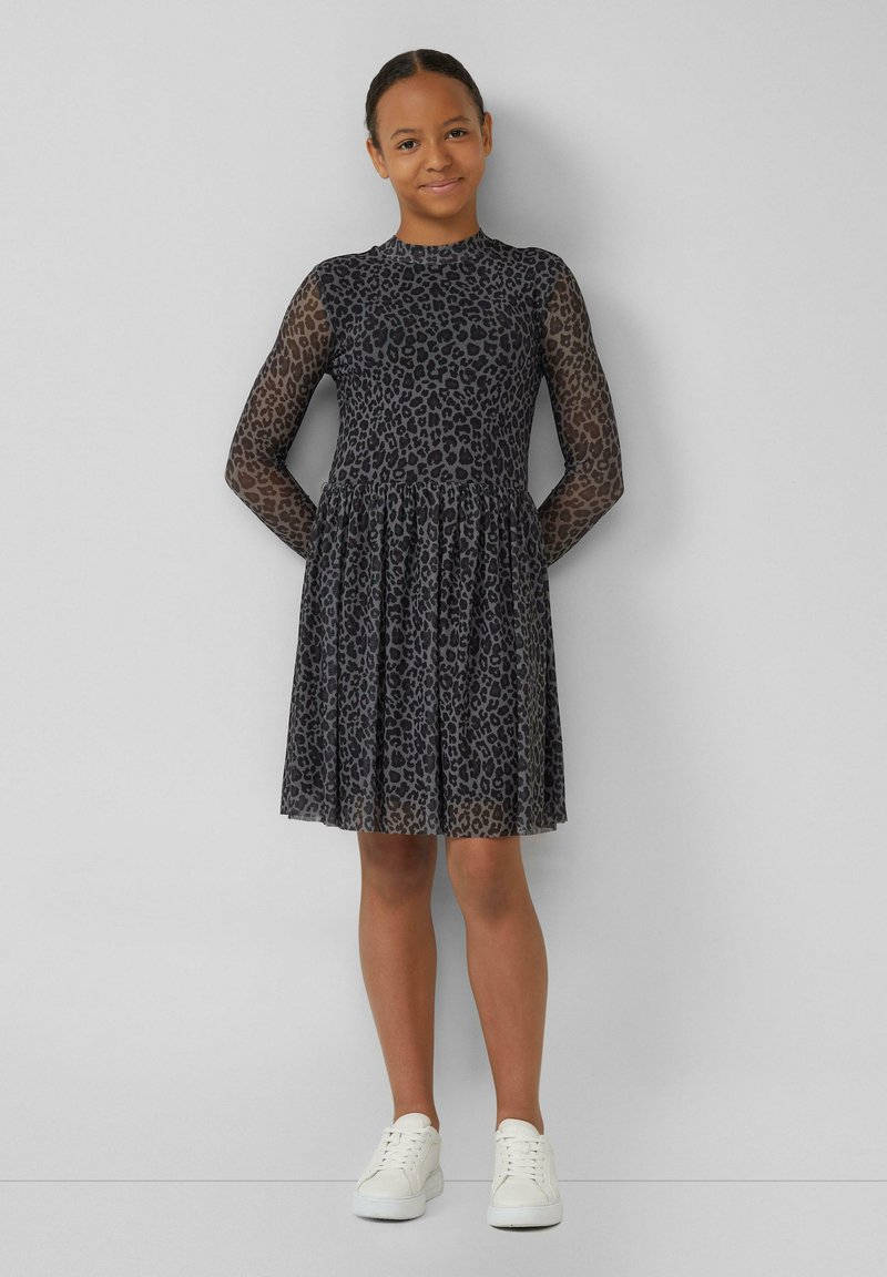 Schwarzes Leopardenmuster-Kleid mit langen, transparenten Netzärmeln und einem gerafften Rock; kombiniert mit weißen Sneakers. Glatte Stoffstruktur.
