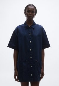 Tengerészkék rövid ujjú ing, gombos záródással, mellkaszsebekkel és hegyes gallérral. Texturált anyagból készült.