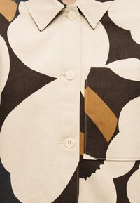 Prednji dio košulje s velikim apstraktnim cvjetnim uzorkom u bež, smeđoj i crnoj boji, s gumbima, ovratnikom i kvadratnim džepom na desnoj strani.