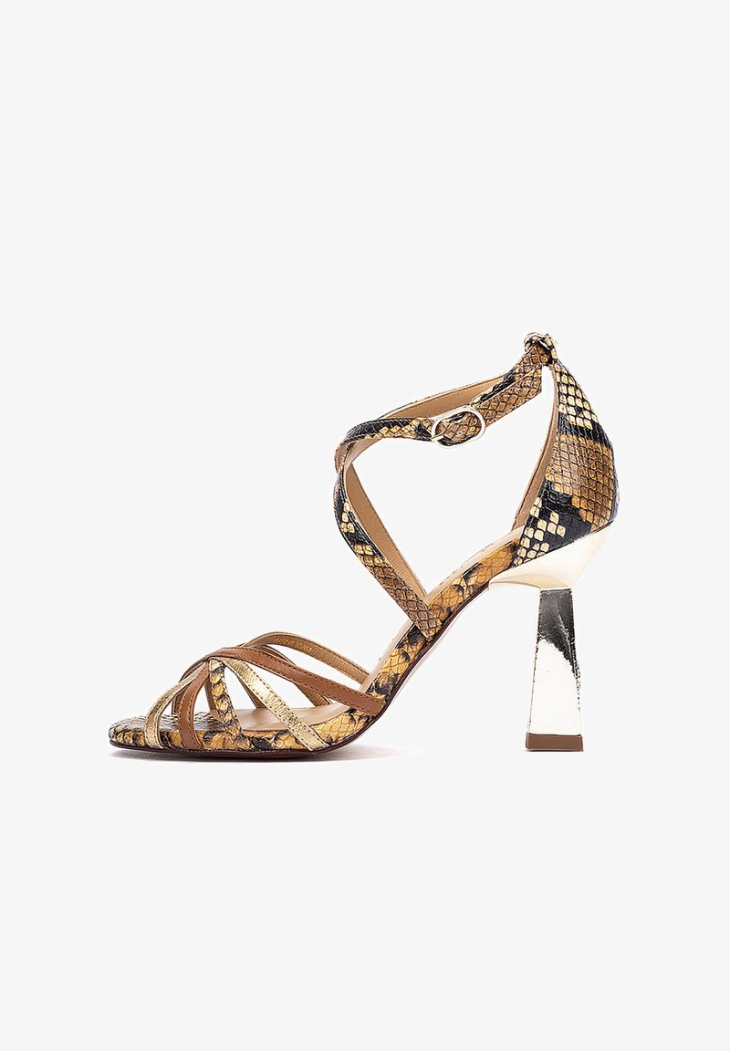 Sandale à talon haut avec des lanières en peau de serpent dorée, marron et noire, talon bloc argenté et bride à la cheville avec fermeture à boucle sur fond blanc.