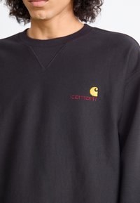 Zwarte sweatshirt van gestructureerde stof, met een ronde halslijn, geribde manchetten en een geborduurd logo in geel en bordeaux.