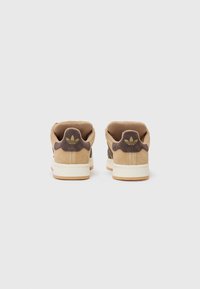 Brown suede sneakers with a cream rubber sole, featuring a textured design, cushioned collar, and gold logo detail on the heel.