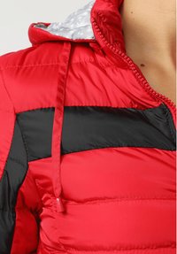 Chaqueta acolchada roja y negra con forro gris estampado, que incluye una cremallera, capucha con cordón y textura acolchada en un diseño de capas.