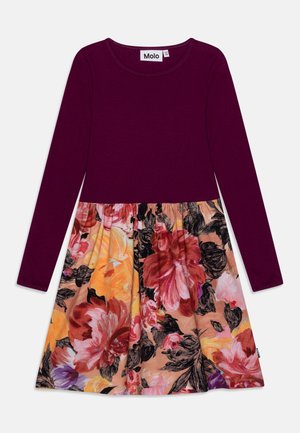 Langærmet kjole med en lilla top og et sammensyet nederdel med blomsterprint i nuancer af pink, orange og sort på en beige baggrund.