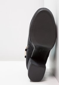 Bottine en daim noir avec talon bloc, fermeture éclair latérale et semelle extérieure en caoutchouc texturé. La tige présente une finition lisse et un équipement minimal.