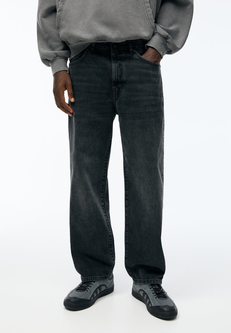 Jeans neri a gamba dritta in denim, con texture sbiadita e design a cinque tasche, abbinati a scarpe da ginnastica grigie.