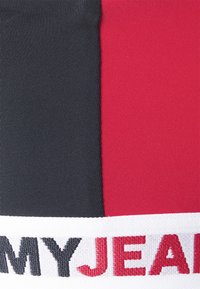 Painel de tecido tricolor com secções em preto, vermelho e branco. A faixa branca apresenta texto em preto e vermelho, "MYJEANS," com uma superfície texturizada.