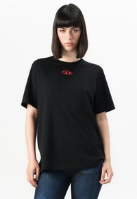 Black short-sleeve t-shirt featuring a red logo on the chest. Soft fabric with a loose fit. Paired with blue denim jeans.