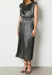 Metallisk silverklänning med vertikala veck, ärmlös design, elastisk midja och längd till mitten av vadderna. Komfortabelt kombinerad med svarta klackskor med remmar.