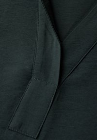 Ciemnozielony materiał o gładkiej fakturze, z dekoltem w kształcie litery V i wyszywaną listwą. Minimalistyczne i czyste linie.