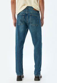 Jeans de mezclilla azul oscuro con un ajuste relajado, que cuentan con cinco bolsillos, un ligero desvanecimiento y un parche de cuero marrón con la marca en la parte trasera de la cintura.