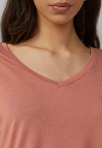 Mīksts, rozā īsām piedurknēm krekls ar V-veida kakla dizainu un gludu tekstūru, izceļot ikdienišķu stilu, kas piemērots dažādām iespējām.