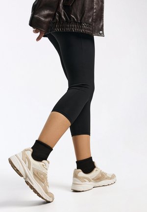 Schwarze Leggings mit eng anliegendem Schnitt, kombiniert mit beigen und cremefarbenen Sportschuhen mit strukturierten Akzenten und Gummisohlen.
