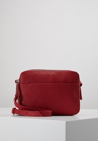 Punainen nahkainen olkalaukku vetoketjulla, litteä muotoilu ja irrotettava olkahihna. Ominaisuuksiin kuuluu sileä pinta ja minimalistiset yksityiskohdat.