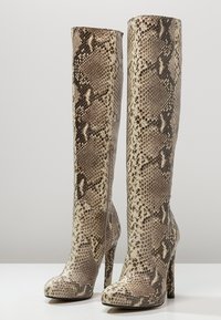 Knee-high heeled boots in beige and brown faux snake skin, featuring a textured pattern and a side zipper for closure.