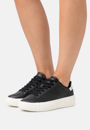 Czarne skórzane sneakersy z białą teksturowaną podeszwą. Posiadają czarne sznurówki, smukły design i srebrny akcent na pięcie. Nazwa marki wytłoczona.