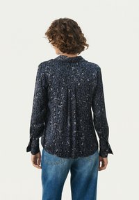 Marineblauwe blouse met luipaardprint, lange mouwen, relaxte pasvorm en knoopsluiting bij de mouwen. Textuurstof met een gladde glans.