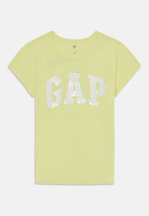 Camiseta de manga corta amarilla claro con un logo "GAP" en lentejuelas blancas en la parte frontal. Tejido suave con cuello redondo y dobladillo recto.