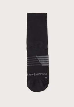 Μία μαύρη κάλτσα με γκρι ρίγες και λογότυπο "new balance" στο πόδι, τοποθετημένη επίπεδα σε λευκό φόντο.