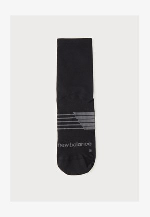 En enkelt sort strømpe med grå striber og "new balance"-logo på foden, lagt fladt mod en hvid baggrund.
