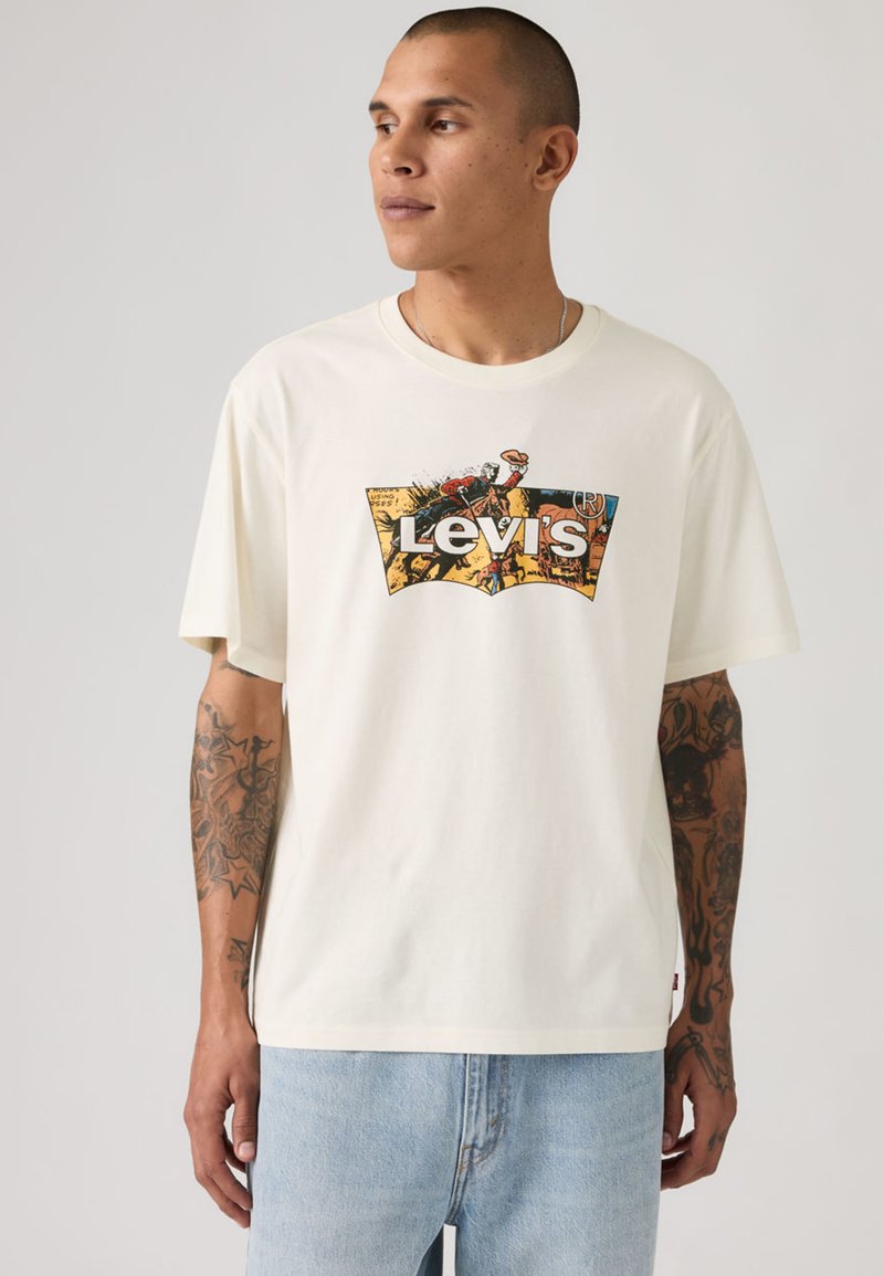 Camiseta de algodón color crema con un logo gráfico colorido de Levi's. Corte relajado, mangas cortas, combinada con vaqueros de mezclilla en un lavado claro.