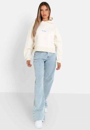 Crème cropped hoodie met borduring aan de voorkant, gecombineerd met lichtblauwe hoge taille jeans. Witte sneakers maken de casual outfit compleet.