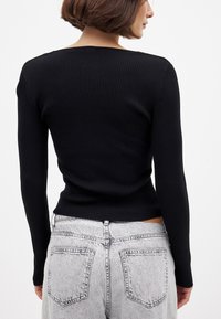Schwarzer gerippter Pullover mit langen Ärmeln, der über einen quadratischen Halsausschnitt und eine figurbetonte Passform verfügt, kombiniert mit hellgrauen Hochbundjeans.
