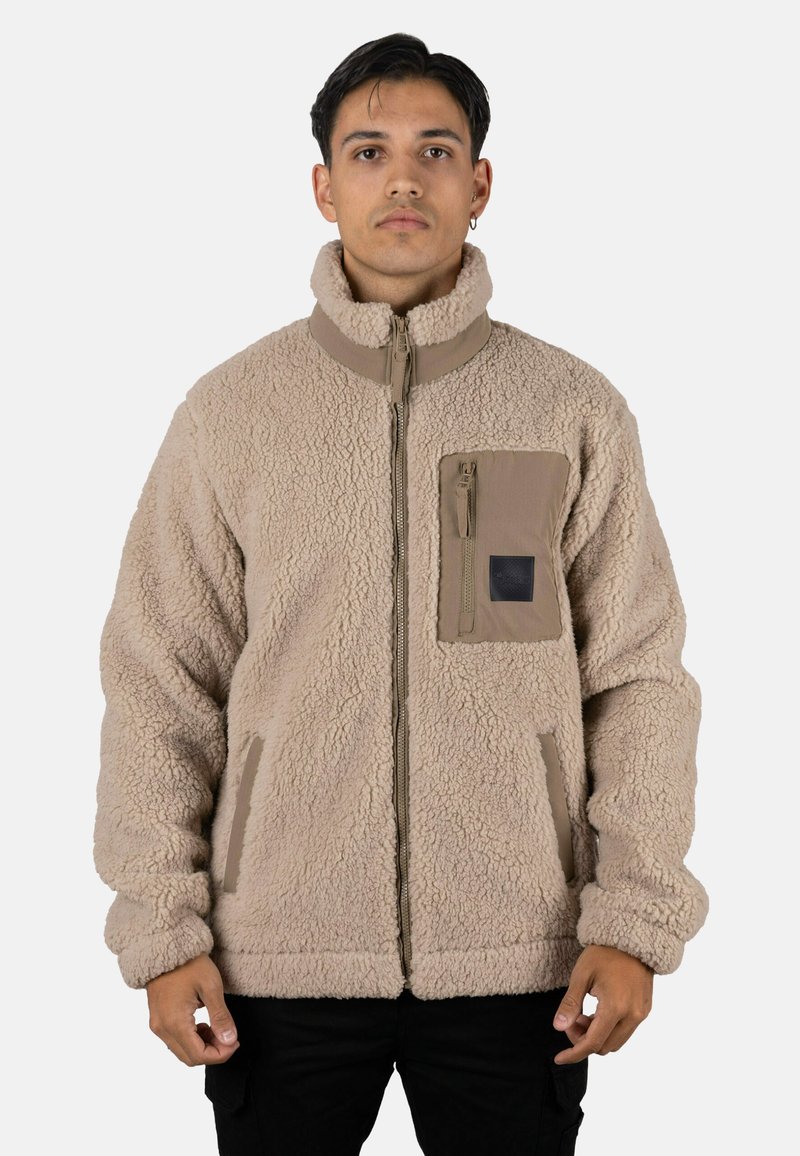 Chaqueta de forro polar en beige claro con cuello alto, cremallera frontal y bolsillos laterales. Cuenta con un bolsillo en el pecho con cremallera y tejido texturizado.