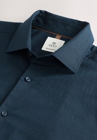 Donkerblauw katoenen regular fit overhemd met een button-down kraag, een borstzak en een contrasterend detail aan het binnenlabel. Twee knopen zichtbaar.