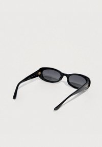 Μαύρα γυαλιά ηλίου με κομψό οβάλ σχήμα, σκούρους φακούς και γυαλιστερό φινίρισμα. Λογότυπο "Vogue" σε χρυσό στο εξωτερικό μέρος των βραχιόνων.