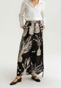 Černá maxi sukně s botanickým potiskem v krémové barvě, s vysokým pasem, bočními kapsami a uvolněným, splývavým střihem.
