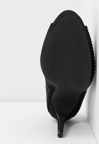 Musta mokkanahkasta valmistettu korkokenkä, jossa on terävä kärki, teksturoitu päällinen ja sileä pohja. Korkeuden vaikutelma on nostettu.