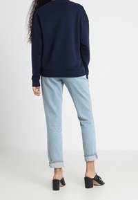 Sudadera azul marino con puños acanalados, combinada con jeans de denim azul claro, remangados en el dobladillo. Mules de tacón negro completan el atuendo.