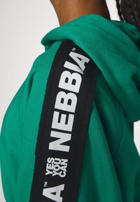 Felpa verde con tessuto testurizzato; presenta una striscia laterale nera con il testo bianco "YES YOU CAN NEBBIA" e un design con cappuccio.