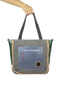 Bolsa de mano multicolor con felpa gris texturizada, bolsillo delantero de nailon azul, lados verdes y acento circular amarillo. Asas de tela gris resistente.