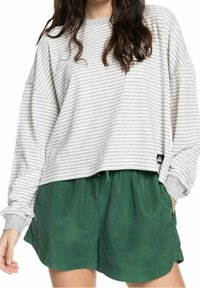 Grau-weißer gestreifter Langarmshirt mit lockerer Passform; kombiniert mit grünen Shorts mit elastischem Bund und Taschen.