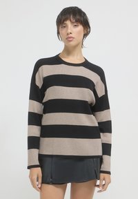 Schwarz-beige gestreifter Pullover mit gerippter Textur, Rundhalsausschnitt und langen Ärmeln, kombiniert mit einem schwarzen Lederminirock.