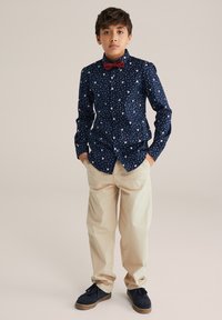 Mornarska srajca s krvavo modrim gumbom in vzorcem pikic ter cvetlic, v kombinaciji s bež hlačami. Rdeča metuljček dopolnjuje obleko; črne čevlje pa dokončajo videz.