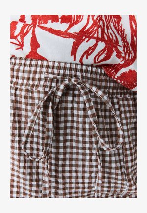 Hnedá a bielo kockovaná látka s elastickým pásom a viazanou šnúrkou. Červený kvetovaný top čiastočne viditeľný nad pásom.