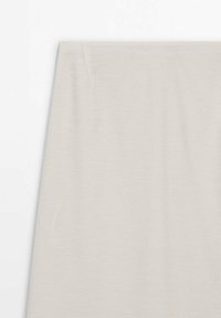 Rideau en tissu beige suspendu droit contre un mur blanc, montrant de légers plis et une texture douce.