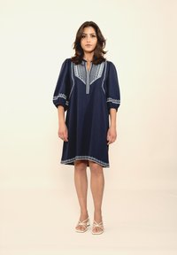 Navyblaues Kleid mit besticktem Ausschnitt und Ärmeln, ausgestattet mit puffartigen Ärmeln und einer lockeren Passform, gesäumt mit detaillierten Floralstickereien.