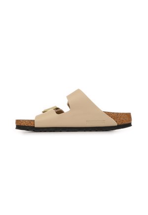 Sandale slide beige Birkenstock avec deux brides réglables, semelle intérieure en liège et semelle noire texturée vue de côté sur fond blanc.