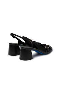 Scarpe slingback in pelle nera con punta arrotondata, dettagli in oro decorativo e tacco spesso. Presentano una suola blu a contrasto.