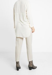 Blusa a maniche lunghe di un leggero color crema con orlo arrotondato e tessuto a trama, abbinata a pantaloni crema a sigaretta e stivaletti alla caviglia con stampa snake.