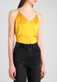 Yellow satin camisole with thin straps, paired with high-waisted black denim jeans and a black belt featuring a rectangular buckle.