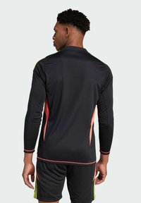 Maglietta sportiva nera a maniche lunghe con dettagli arancioni e verde neon; tessuto a rete; polsini a costine; abbinata a pantaloni corti neri.